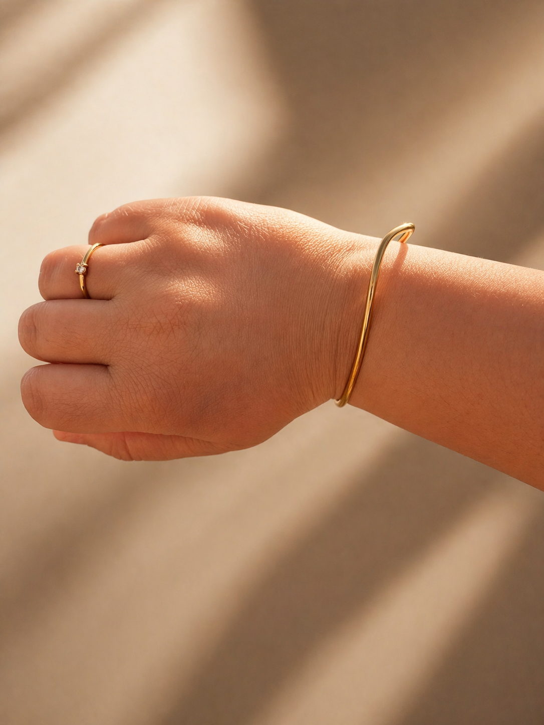 Drift Cuff i 316 kirurgiskt stål och 18k PVD-guld, ett öppet guldfärgat cuff-armband buret på handleden i varmt solljus.