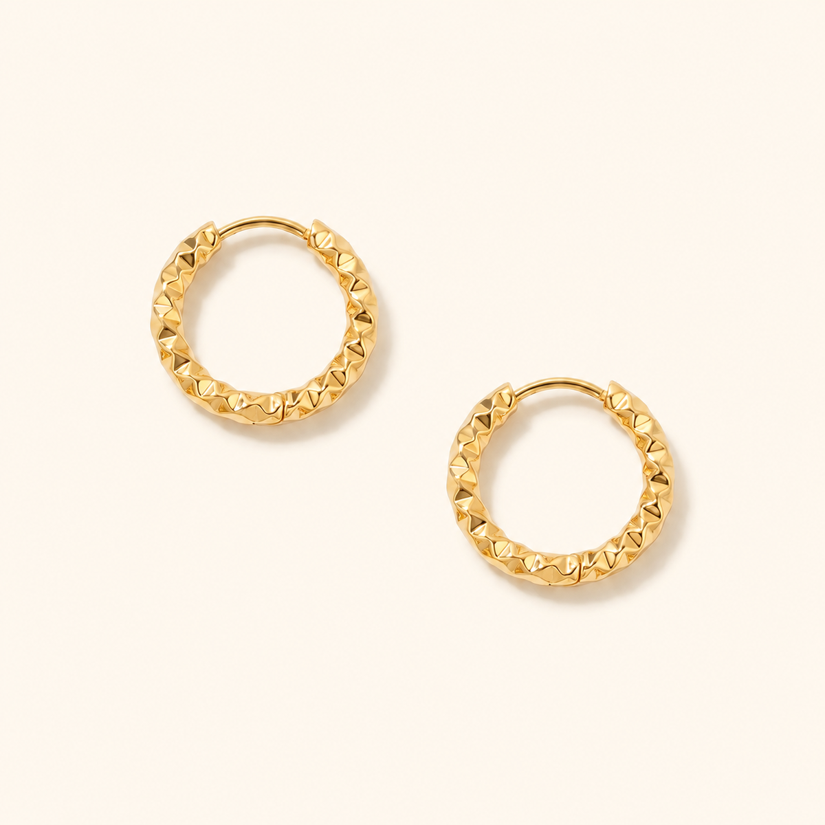 Grain Hoop örhängen i 18k PVD-guld med texturerad rund form på ljus bakgrund.