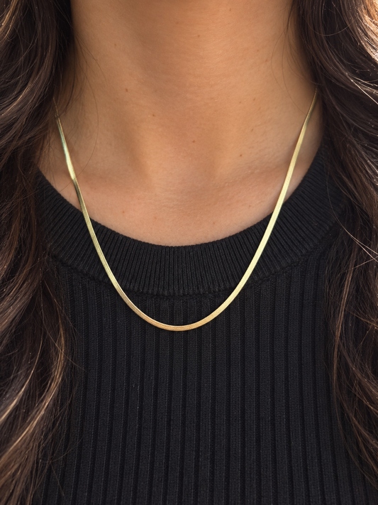 Lune Necklace 1,7mm i guld buren på halsen med svart topp i varmt dagsljus.