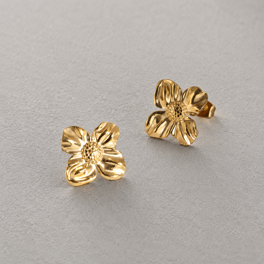 Petal Stud i 316 kirurgiskt stål och 18k PVD-guld, ett par blomformade guldfärgade stud-örhängen mot ljus neutral bakgrund.
