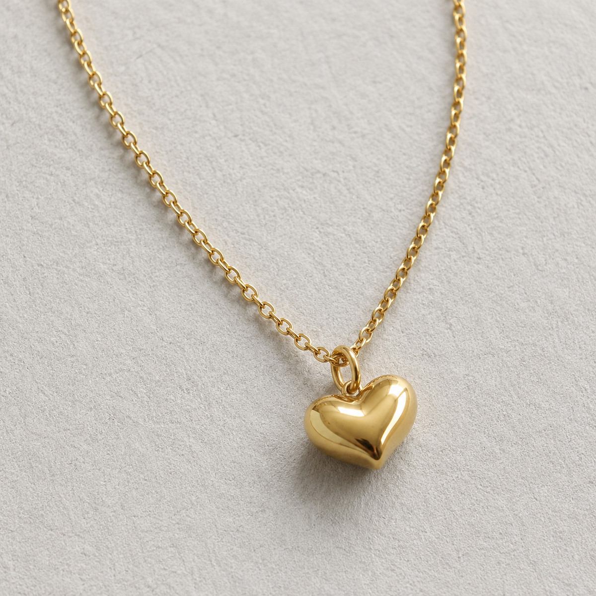 Pulse Necklace 316-kirurginteräksestä, 18K PVD-kultapinnoitteella, lähikuva kullanvärisestä kaulakorusta pyöristetyllä sydänriipuksella vaaleaa neutraalia taustaa vasten.