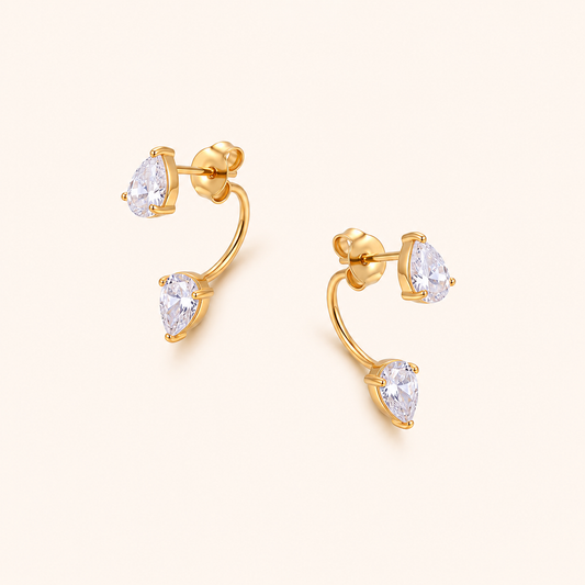 Vela Stud örhängen i 18k PVD-guld med två droppformade zircon och böjd design på ljus bakgrund