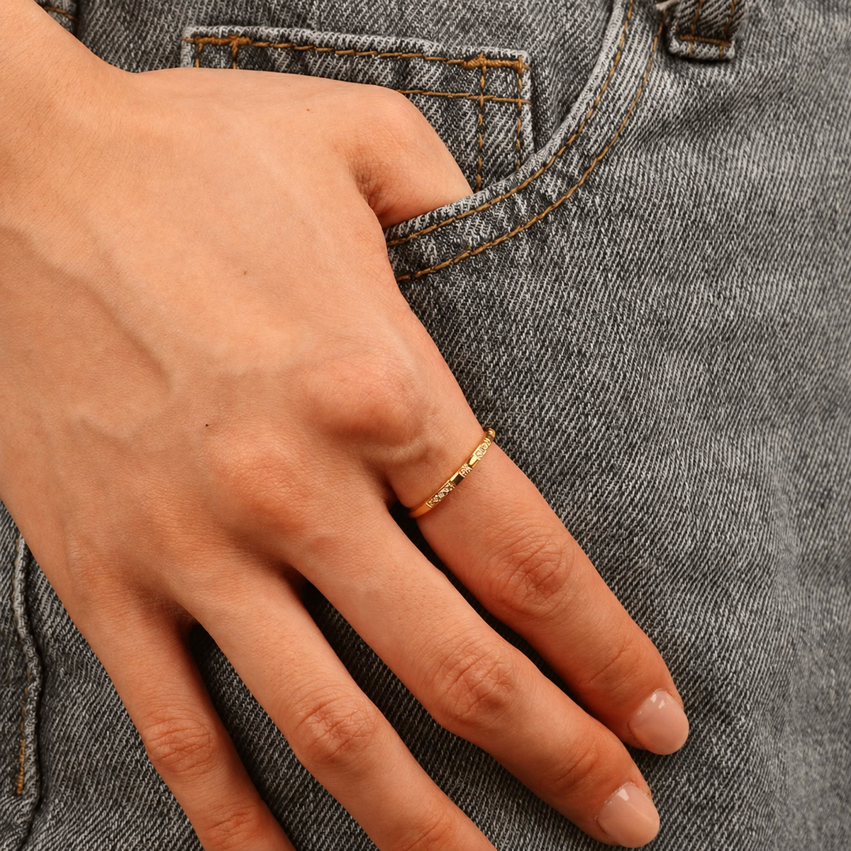 Spark Ring i 316 kirurgiskt stål och 18k PVD-guld, en smal guldring med fina detaljer buren på hand mot grå denim.