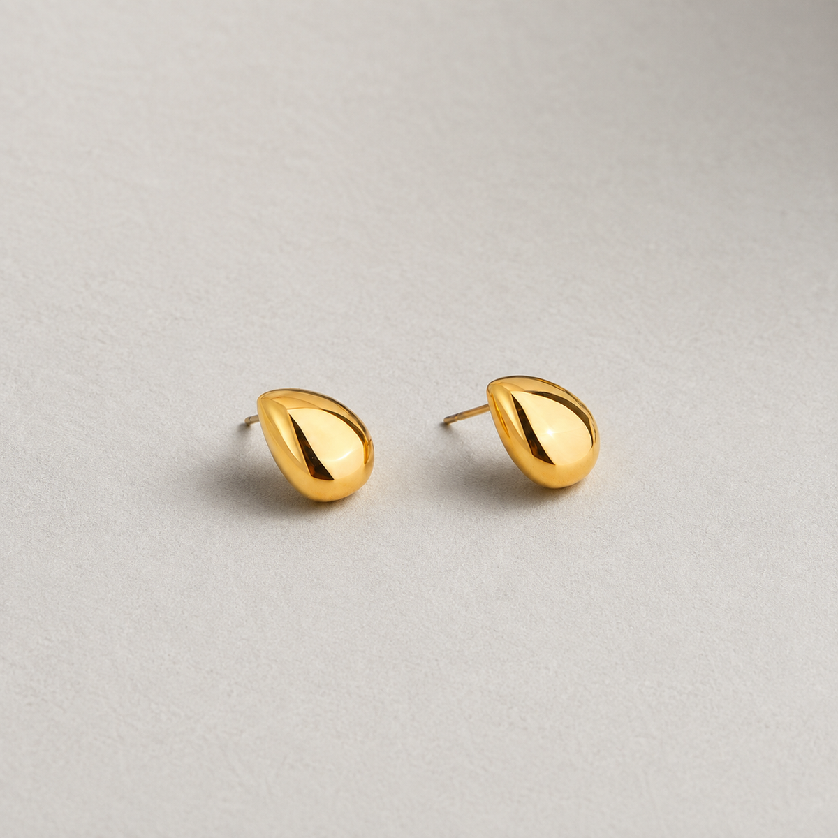 Stone Studs 316-kirurginteräksestä, 18K PVD-kultapinnoitteella, veistokselliset pisarakorvakorut vaaleaa neutraalia taustaa vasten.