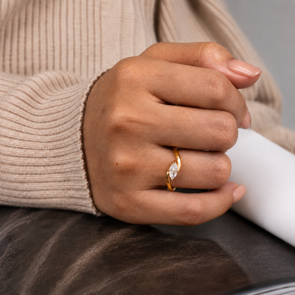 Sway Ring, kullanvärinen sormus kirkkaalla markiisihiontaisella kivellä sormessa beigen neuleen kanssa.