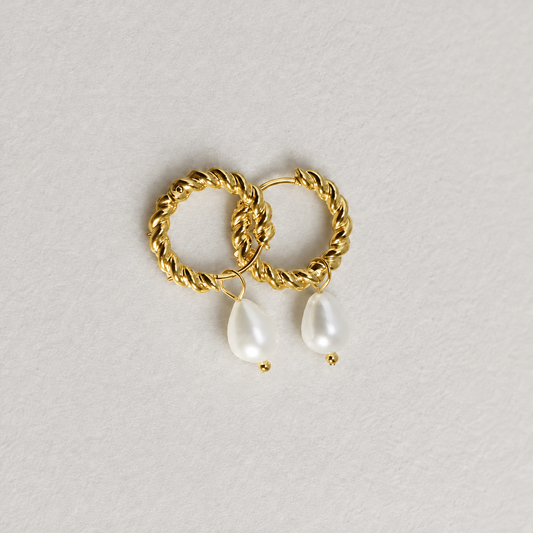 Tide Pearl Hoop 316-kirurginteräksestä, 18K PVD-kultapinnoitteella, kierretyt kullanväriset rengaskorvakorut riippuvilla helmillä vaaleaa neutraalia taustaa vasten.